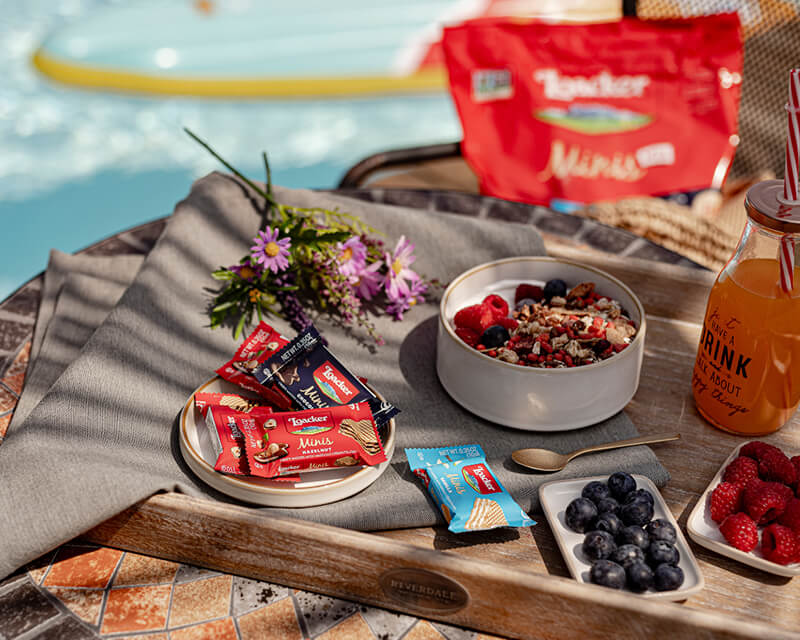 Outdoor setting with Loacker Minis, snacks, berries, and drinks by a poolside.