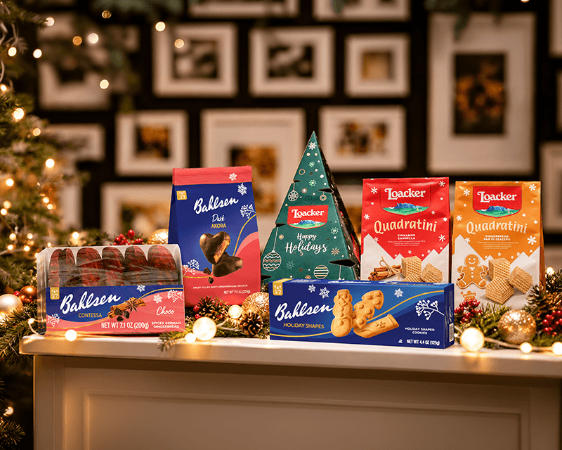 Festive Bahlsen and Loacker holiday cookie and wafer assortment arranged on a table with a Christmas tree, glowing lights and gold ornaments.