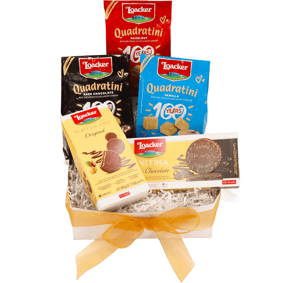 Loacker chocolate and wafer gift basket featuring Quadratini Hazelnut, Vanilla and Dark Chocolate wafers, Tortina Mini Original and Tortina Dark Chocolate, presented with white crinkle paper and a gold bow.