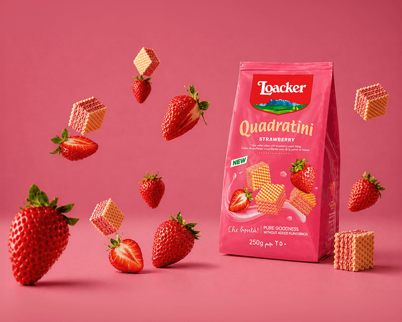 Pink Loacker Quadratini strawberry wafer package amidst floating wafers and strawberries on a pink background, conveying a playful and vibrant tone.