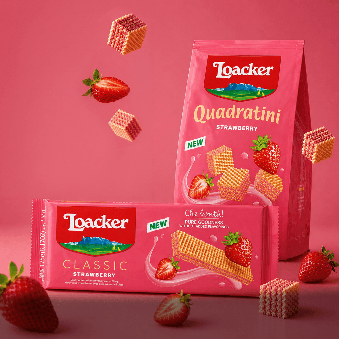 Packaging of Loacker strawberry wafers on a pink background. Includes a bag of Quadratini and a Classic bar, surrounded by strawberries and wafer cubes.