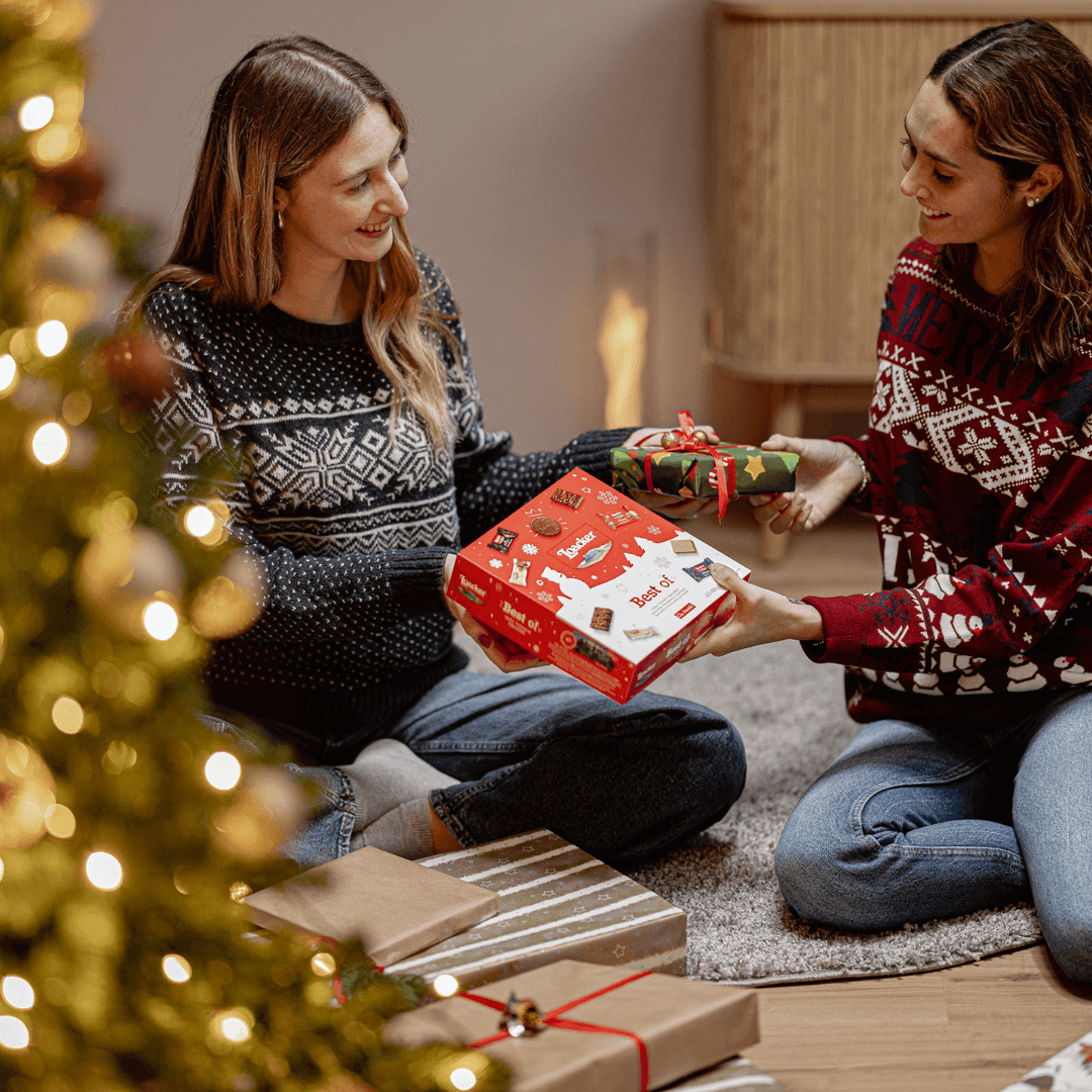 Two women exchanging Christmas presents in a cozy living room with a decorated tree.