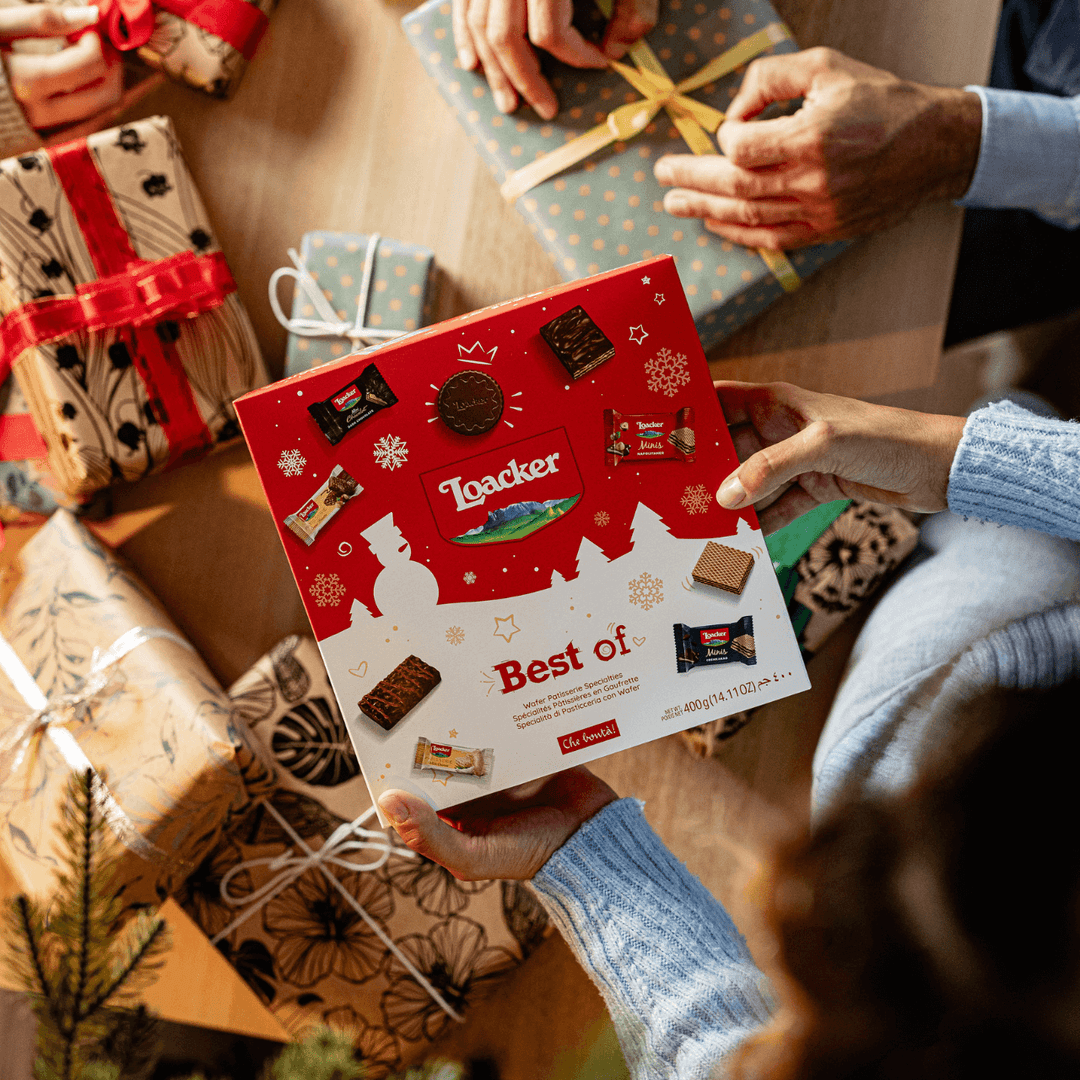 Loacker chocolate box held by a person with wrapped gifts in the background