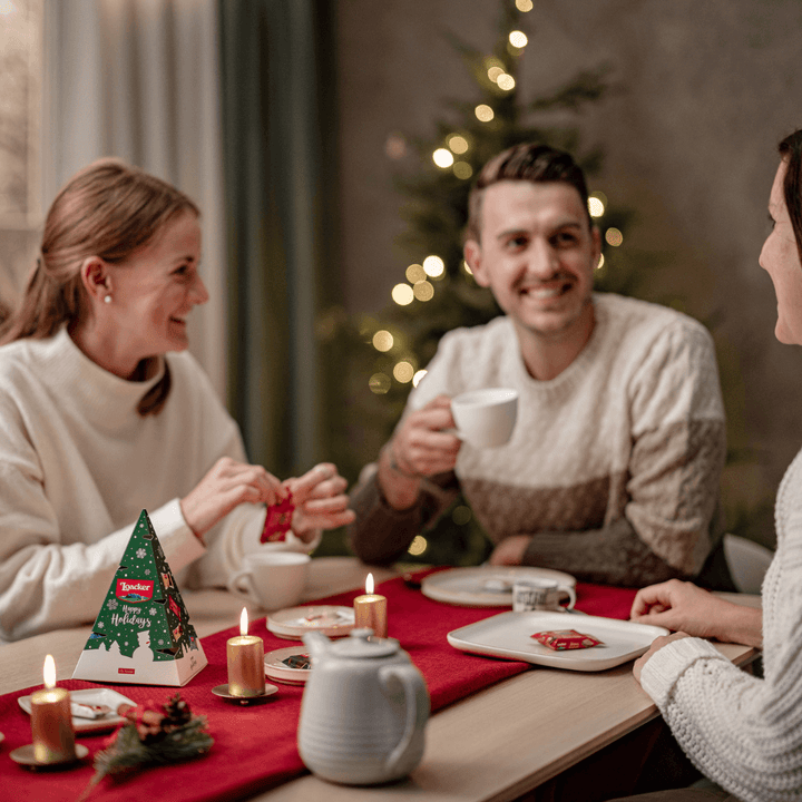 Three people sitting around a table with Christmas decorations, including a tree and lights.