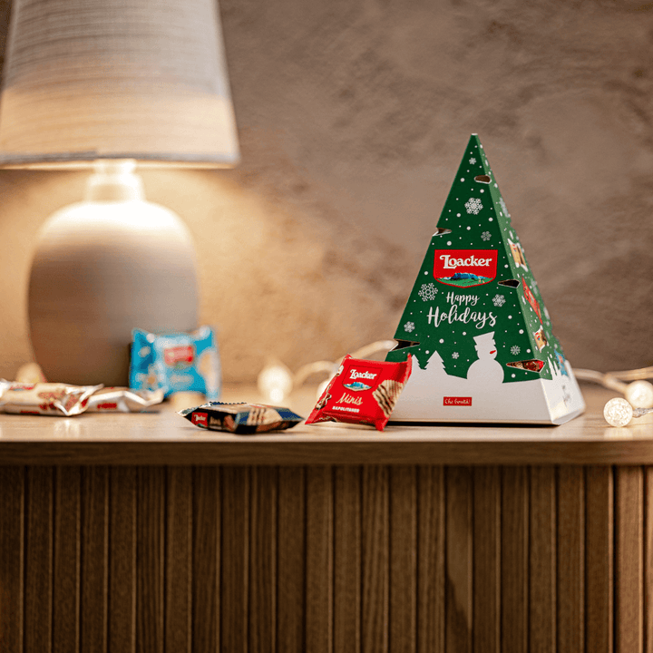 Loacker chocolate box shaped like a Christmas tree on a wooden surface with a lamp in the background.