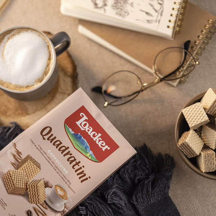 Quadratini Cappuccino, Creme-Filled Wafer Cookies, 7.76 oz. Bag with coffee and glasses in the background
