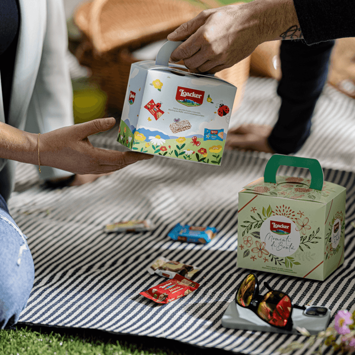 Men passing Loacker Spring Box, Premium Wafer & Chocolate Specialties, 8.67 oz. Box to another person on picnic mate.