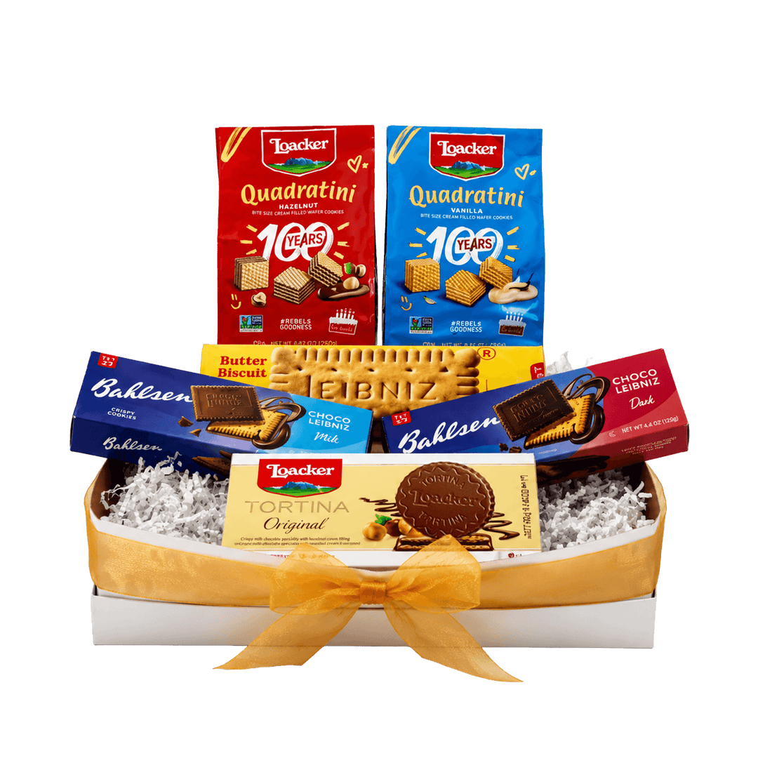 A gift box of assorted Italian snacks and biscuits from La Trocére, arranged in a white tray with white crinkle paper filler and tied with a yellow ribbon. Visible products include boxes of Quadratini, Butter Biscuits, Bahlsen Dark and Milk Chocolate and Tortina Original.