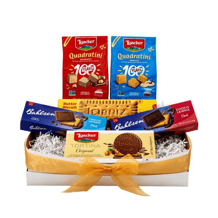 A gift box of assorted Italian snacks and biscuits from La Trocére, arranged in a white tray with white crinkle paper filler and tied with a yellow ribbon. Visible products include boxes of Quadratini, Butter Biscuits, Bahlsen Dark and Milk Chocolate and Tortina Original.